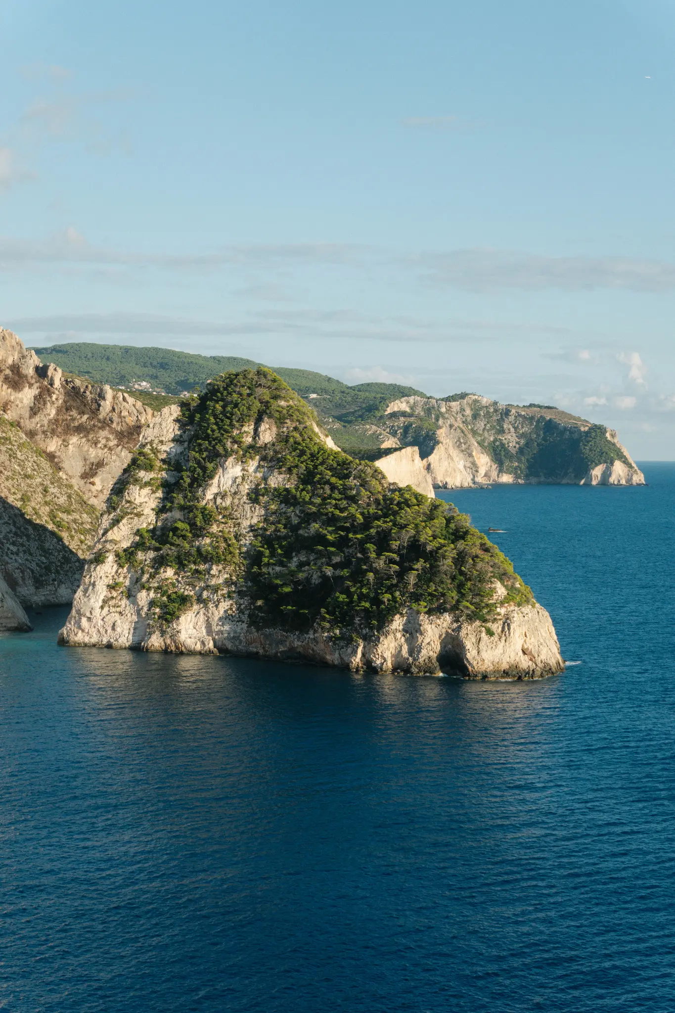 Eine Luftaufnahme einer großen, felsigen Insel, bedeckt mit dichten grünen Bäumen, umgeben von tiefblauem Meer unter einem