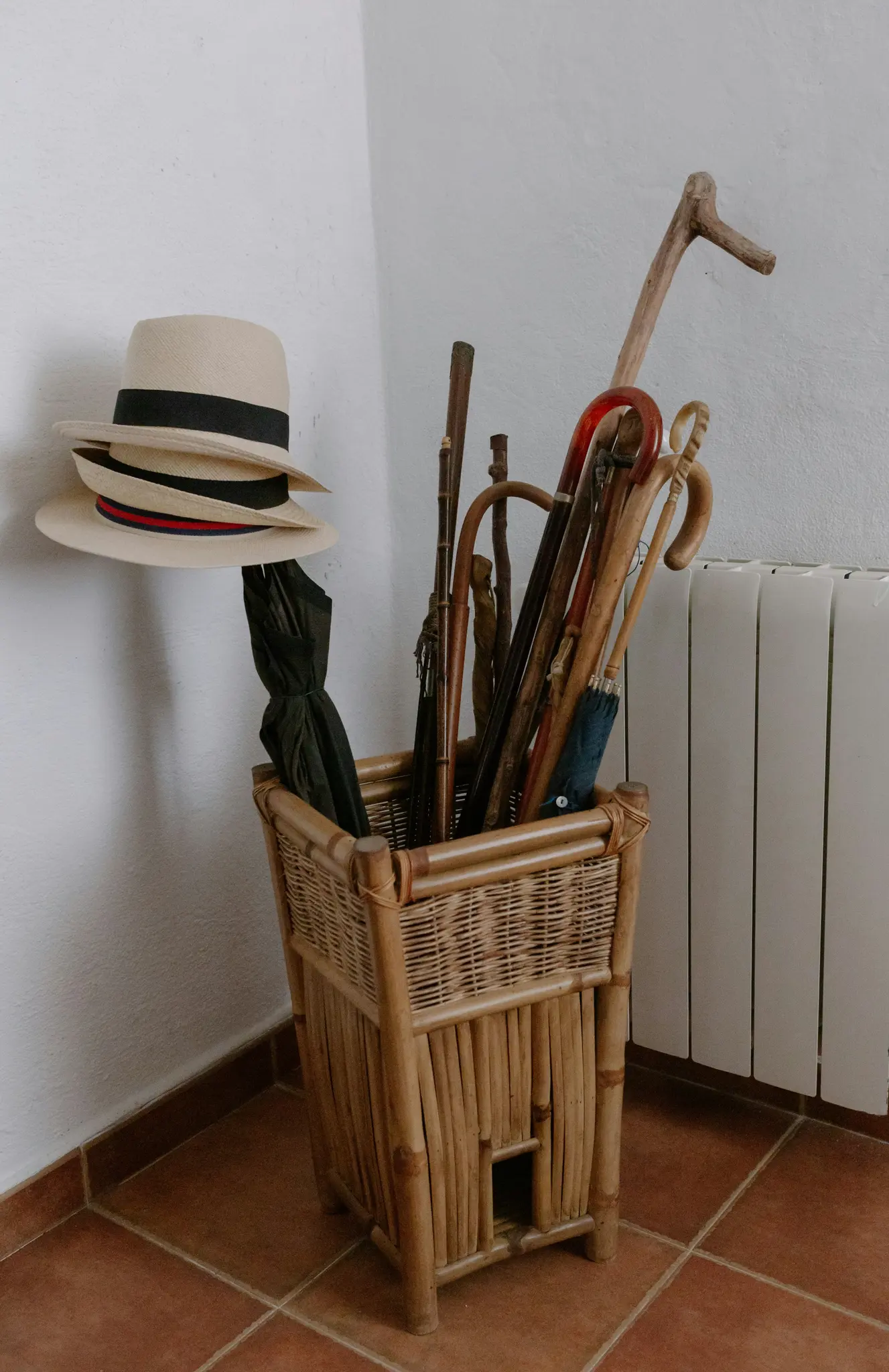 Wiklinowy stojak zawiera dwa słomkowe kapelusze, czarny parasol, niebieski parasol oraz kilka lasek i lasek.