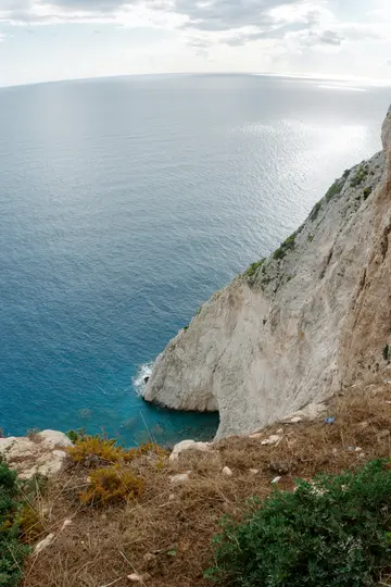 Μια ευρυγώνια λήψη από ψηλά μιας λευκής πλαγιάς που κατεβαίνει σε βαθιά μπλε και τιρκουάζ νερά κάτω από συννεφιασμένο ουρανό.