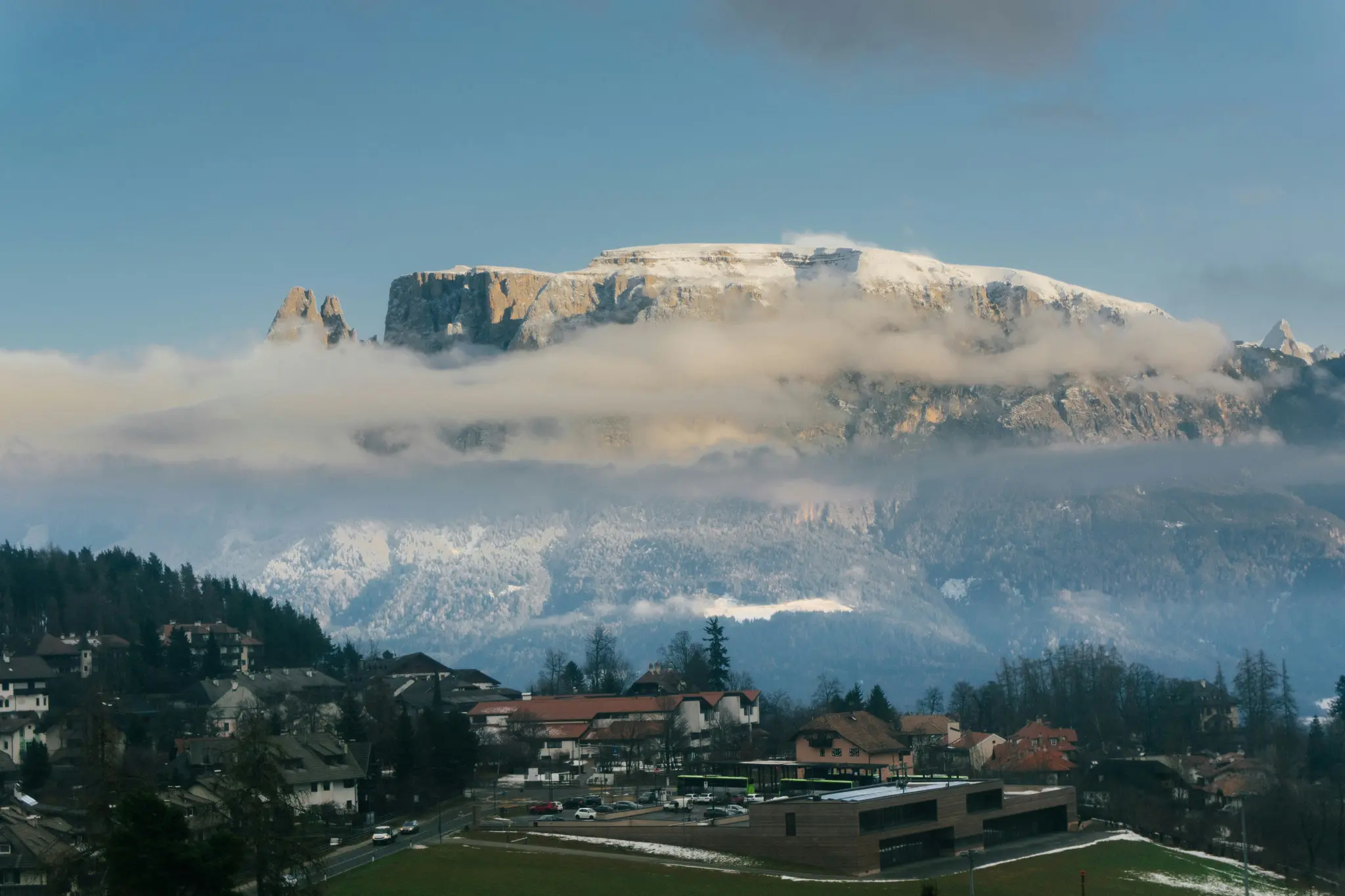 Een weids landschapsbeeld van een dorp in een vallei, met besneeuwde bergen die gedeeltelijk bedekt zijn met wolken op de