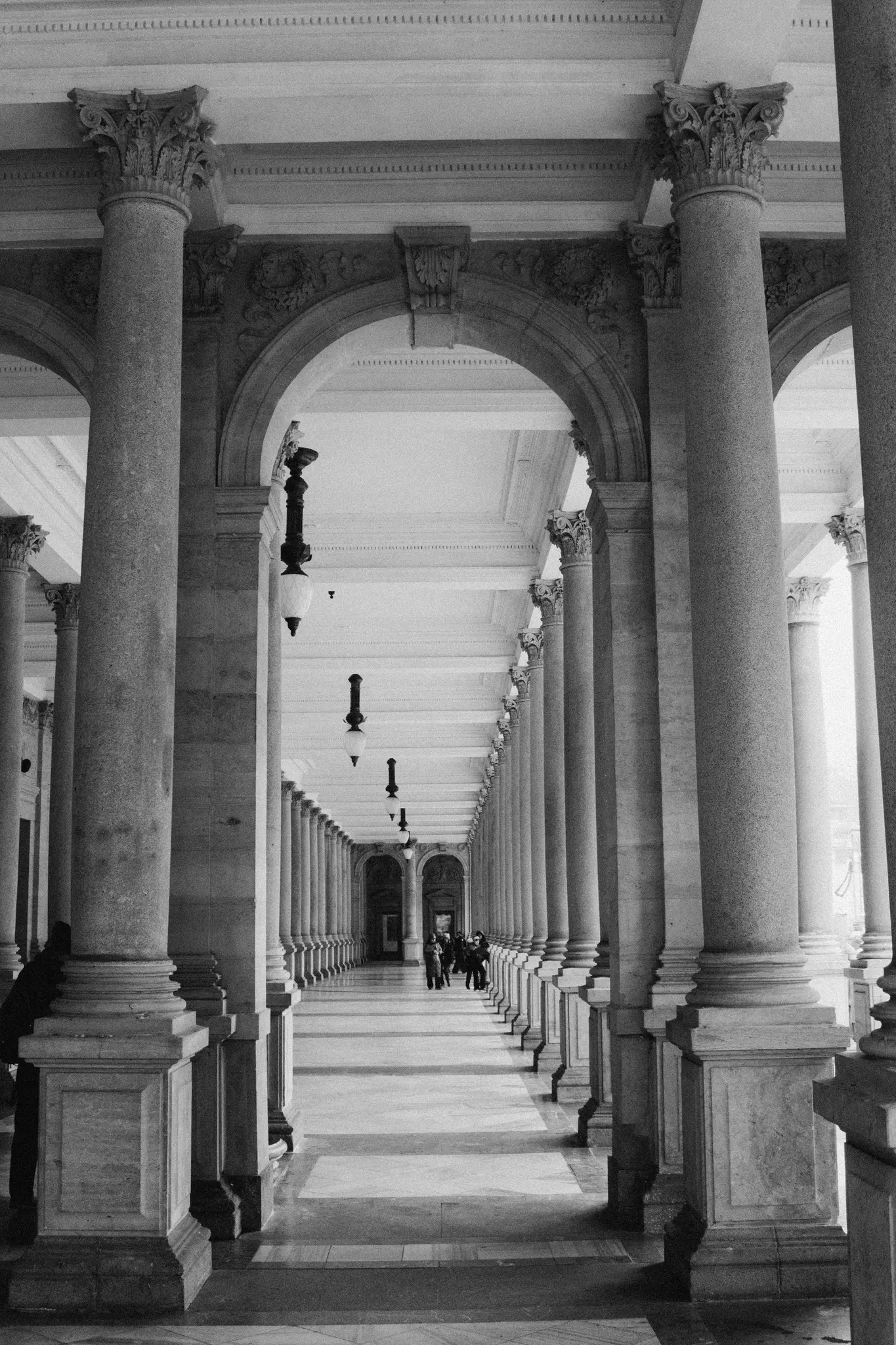 Una foto in bianco e nero di un lungo corridoio ornato fiancheggiato da numerose colonne e archi, che si perde in lontananza.