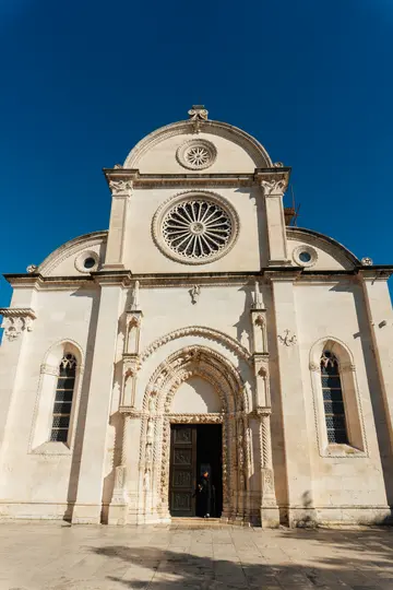 Vue en contre-plongée d'une façade d'église en pierre, grandiose et de couleur claire, avec des sculptures complexes et une