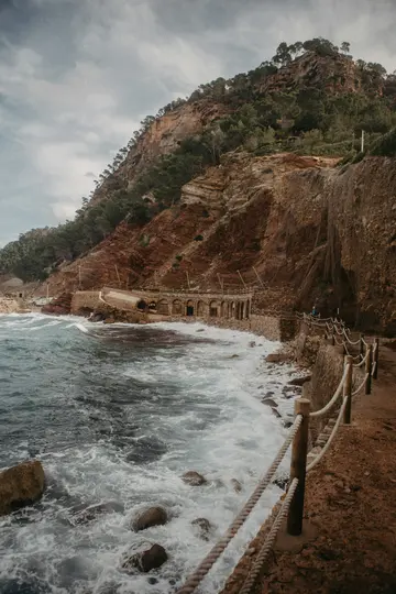Un tortuoso sentiero costiero con una ringhiera in corda sulla destra costeggia una costa rocciosa e frastagliata dove le