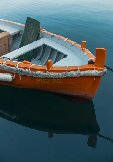 Un barco de pesca de madera con casco naranja y interior azul claro flota sobre agua tranquila de color azul oscuro. El barco