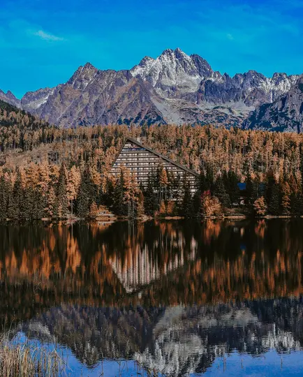 Un remarquable bâtiment A-frame se dresse au milieu d'une forêt d'arbres d'automne orange et marron, se reflétant dans un lac