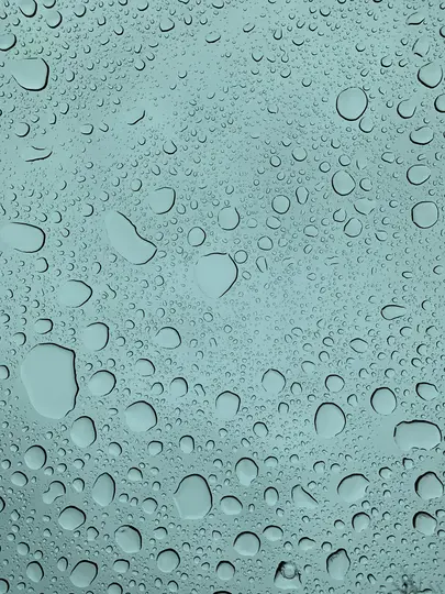 Una vista cercana y abstracta de numerosas gotas de agua transparentes de varios tamaños adheridas a una superficie azul