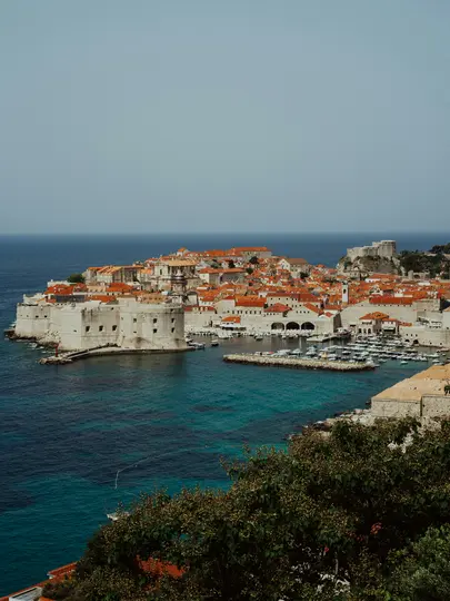 Una vista aerea di una storica città costiera con numerosi edifici con tetti di tegole rosse, un porto vivace con barche…