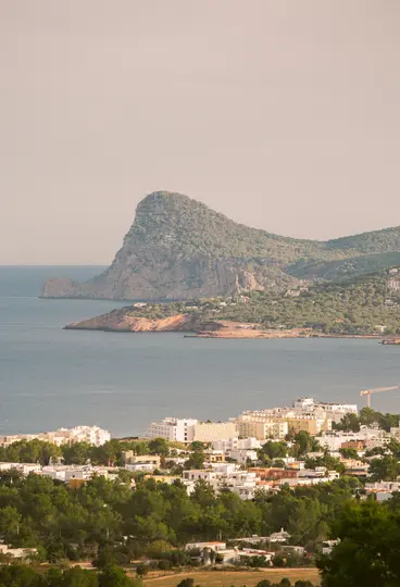 Μια υπερυψωμένη θέα μιας παραθαλάσσιας πόλης με λευκά κτίρια και πράσινα δέντρα, που βλέπει σε έναν κόλπο με ένα μεγάλο
