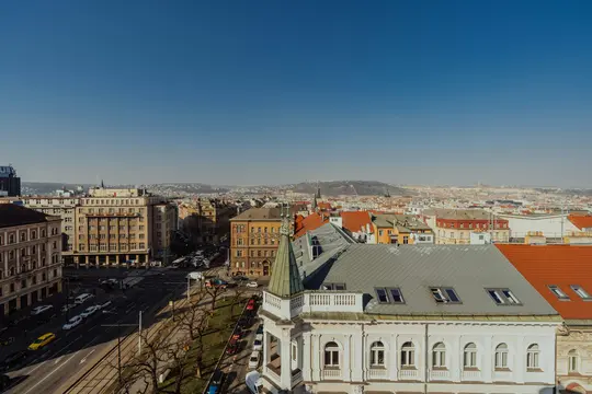 Letecký pohled na město pod jasně modrou oblohou, ukazující širokou ulici, historické budovy s červenými a šedými střechami