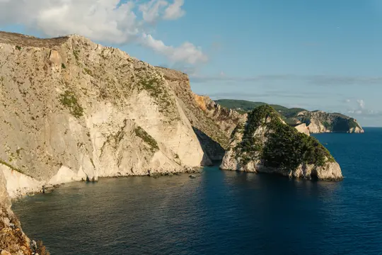 Μια ευρεία πανοραμική άποψη με επιβλητικούς, ανοιχτόχρωμους βράχους καλυμμένους με αραιή πράσινη βλάστηση που συναντούν τη