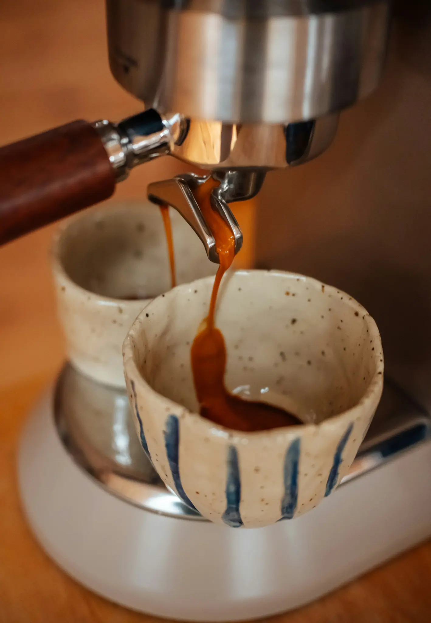 Een close-up van rijke, donkere espresso die uit de portafilter van een machine in twee handgemaakte keramische kopjes