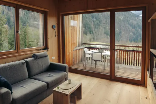 Ein gemütliches Kabinenwohnzimmer mit hellen Holzwänden und -boden, einem grauen Sofa und einem Couchtisch aus Holz. Große