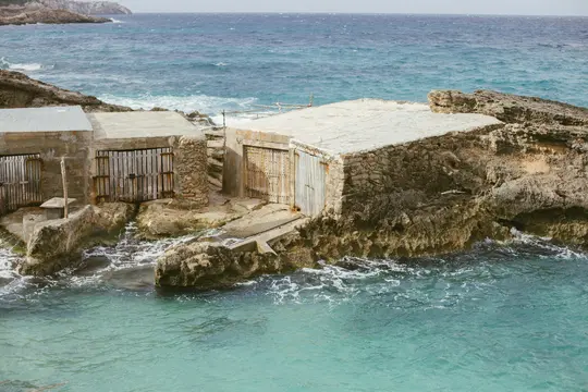 Un'ampia foto paesaggistica di diverse strutture erose in pietra e cemento integrate in una costa rocciosa e aspra. Il mare…