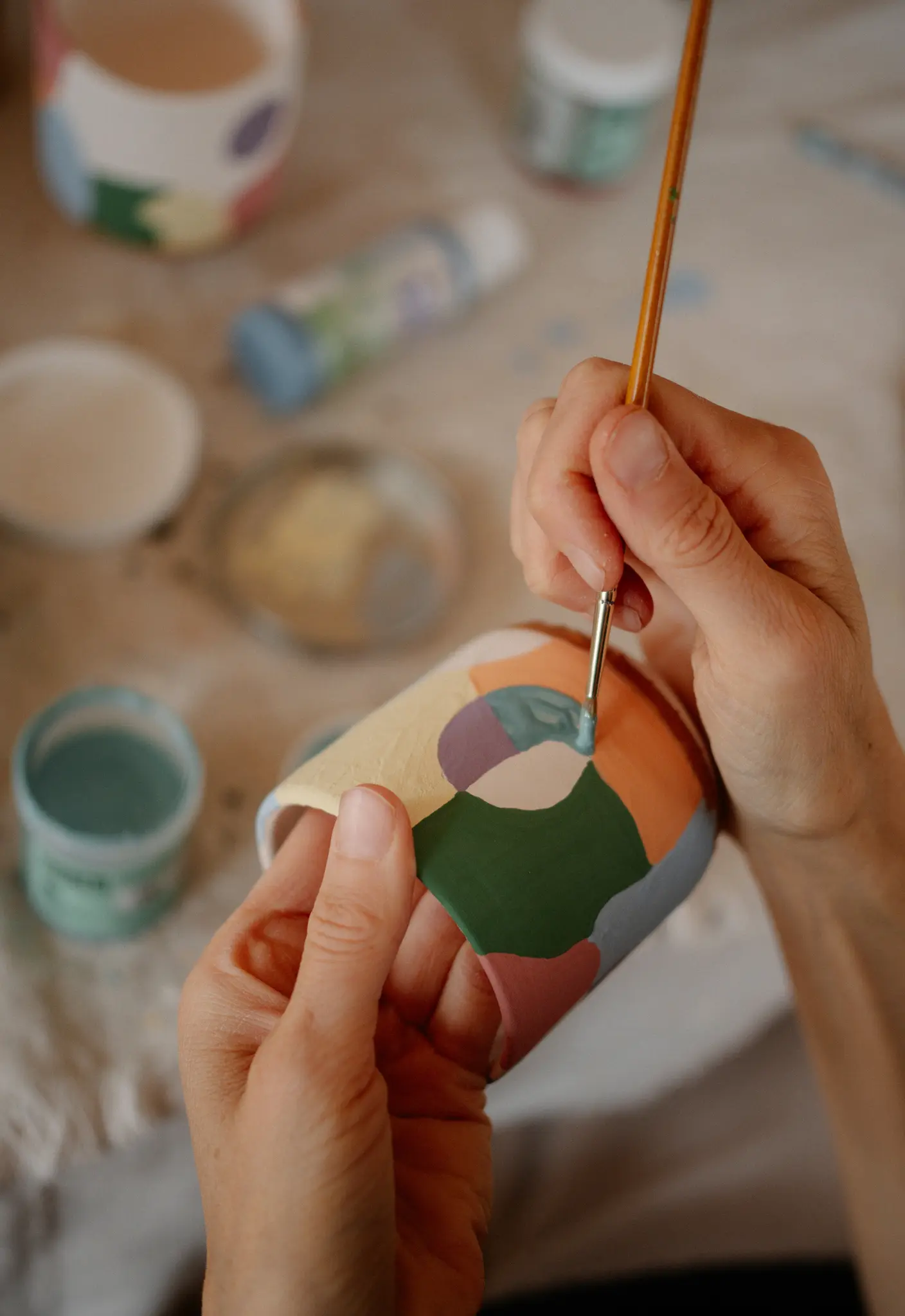 Gros plan sur des mains peignant une tasse en céramique avec un pinceau, appliquant de la peinture bleu clair sur un design