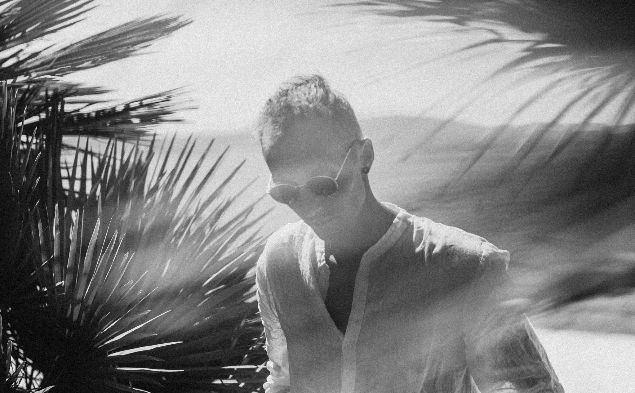 Gros plan moyen en noir et blanc d'une personne aux cheveux courts et portant des lunettes de soleil, regardant vers le bas