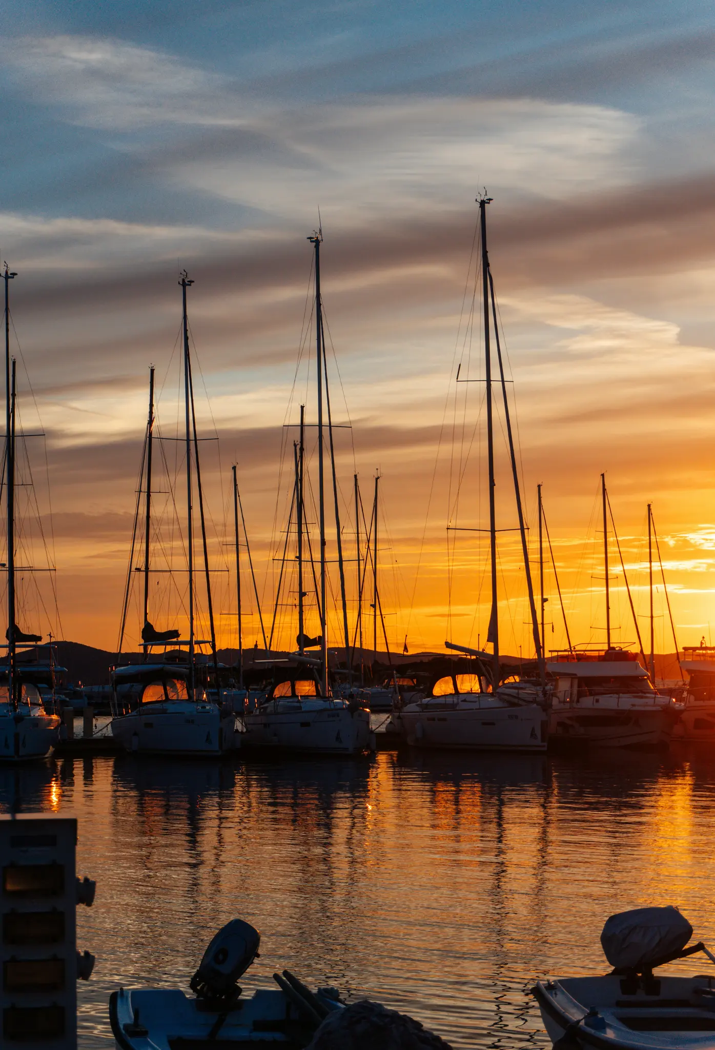 Un coucher de soleil vibrant sur une marina, projetant des teintes chaudes orange et jaunes sur le ciel et se reflétant dans