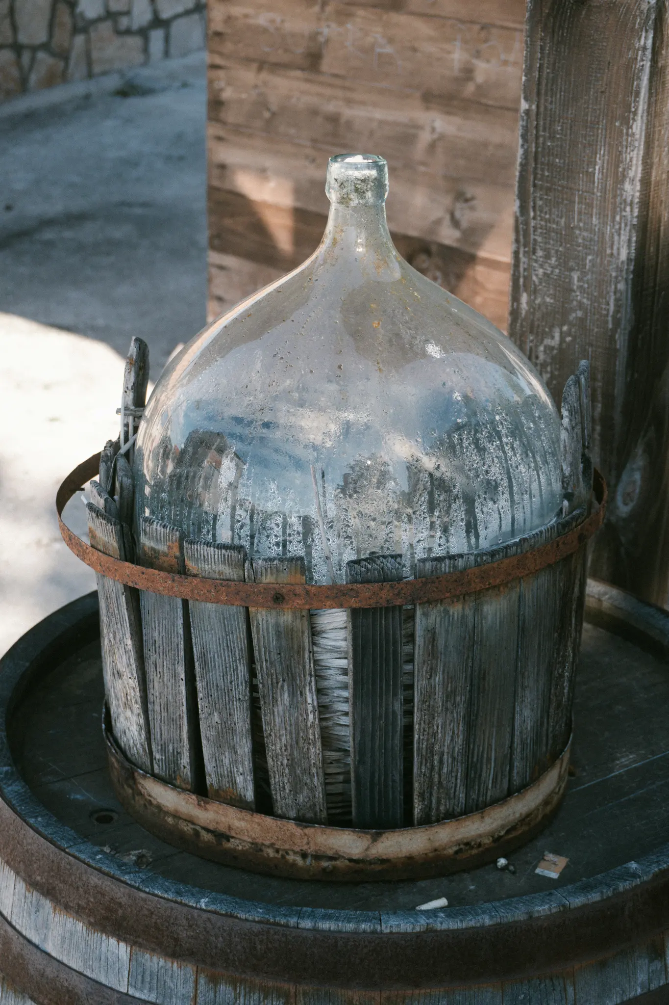 Une grande dame-jeanne en verre poussiéreuse, enveloppée dans un panier en bois vieilli avec des bandes métalliques