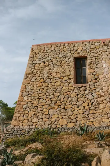 Un rustico edificio in pietra con una singola finestra scura, le sue pareti sono fatte di pietre irregolari marrone chiaro e
