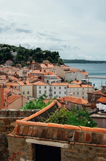 Una vista elevada de un pueblo costero con numerosos edificios con tejados de terracota anaranjados, árboles verdes y un mar