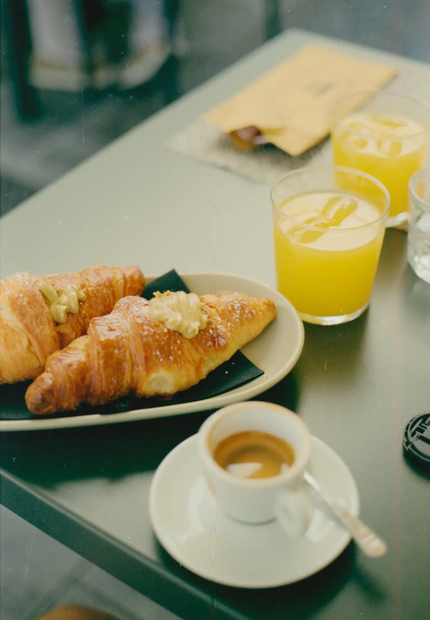 Een close-up van een ontbijttafel met twee croissants, twee glazen sinaasappelsap en een kopje espresso.