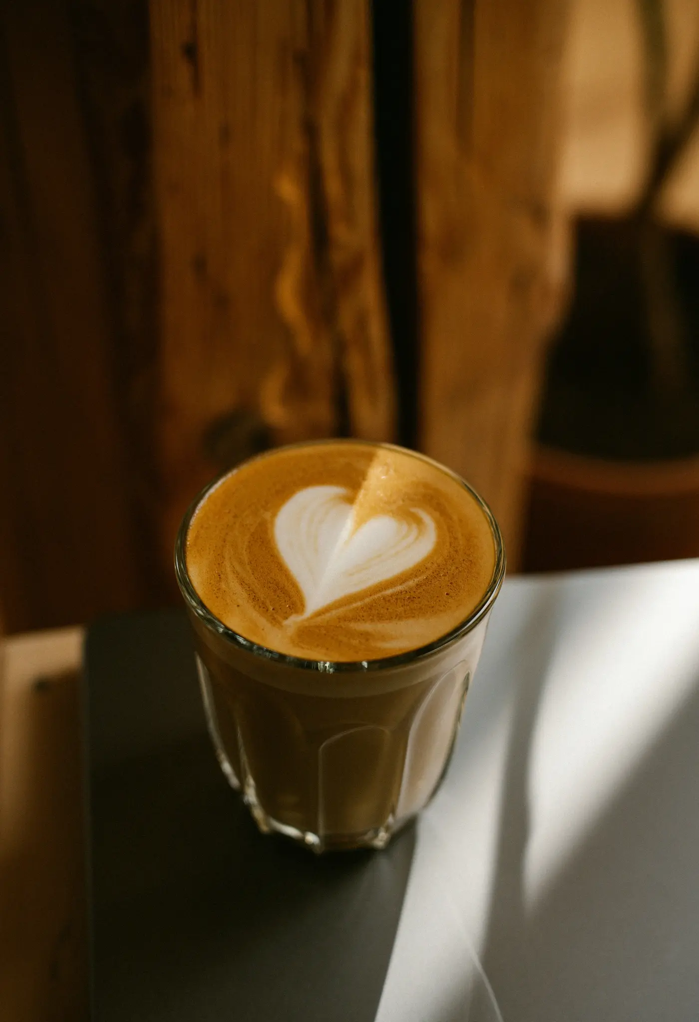 Een helder glas gevuld met latte, met een perfect gevormd wit hart in het schuim, staat op een donker oppervlak.