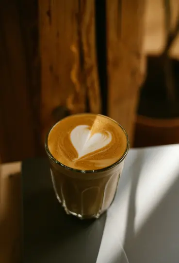 Un bicchiere trasparente pieno di latte, con un cuore bianco perfettamente formato nella schiuma, posa su una superficie