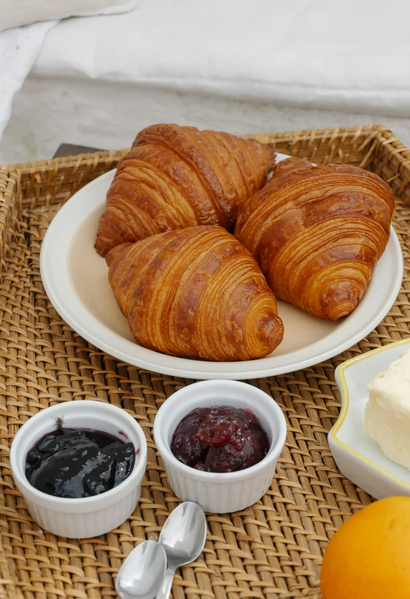 Närbild, en bild ovanifrån av en frukostbricka med tre gyllenbruna croissanter på en vit tallrik, två små skålar med sylt,...