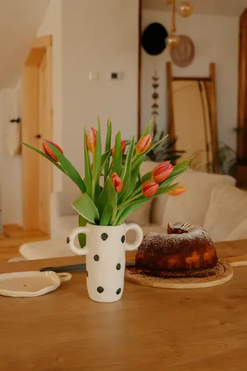 Un vaso bianco a pois neri contiene un bouquet di tulipani arancioni e rossi accanto a una torta Bundt cosparsa di zucchero a