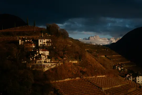 Eine dramatische Landschaftsaufnahme eines Dorfes am Hang mit terrassierten Weinbergen unter einem dunklen, bewölkten Himmel.