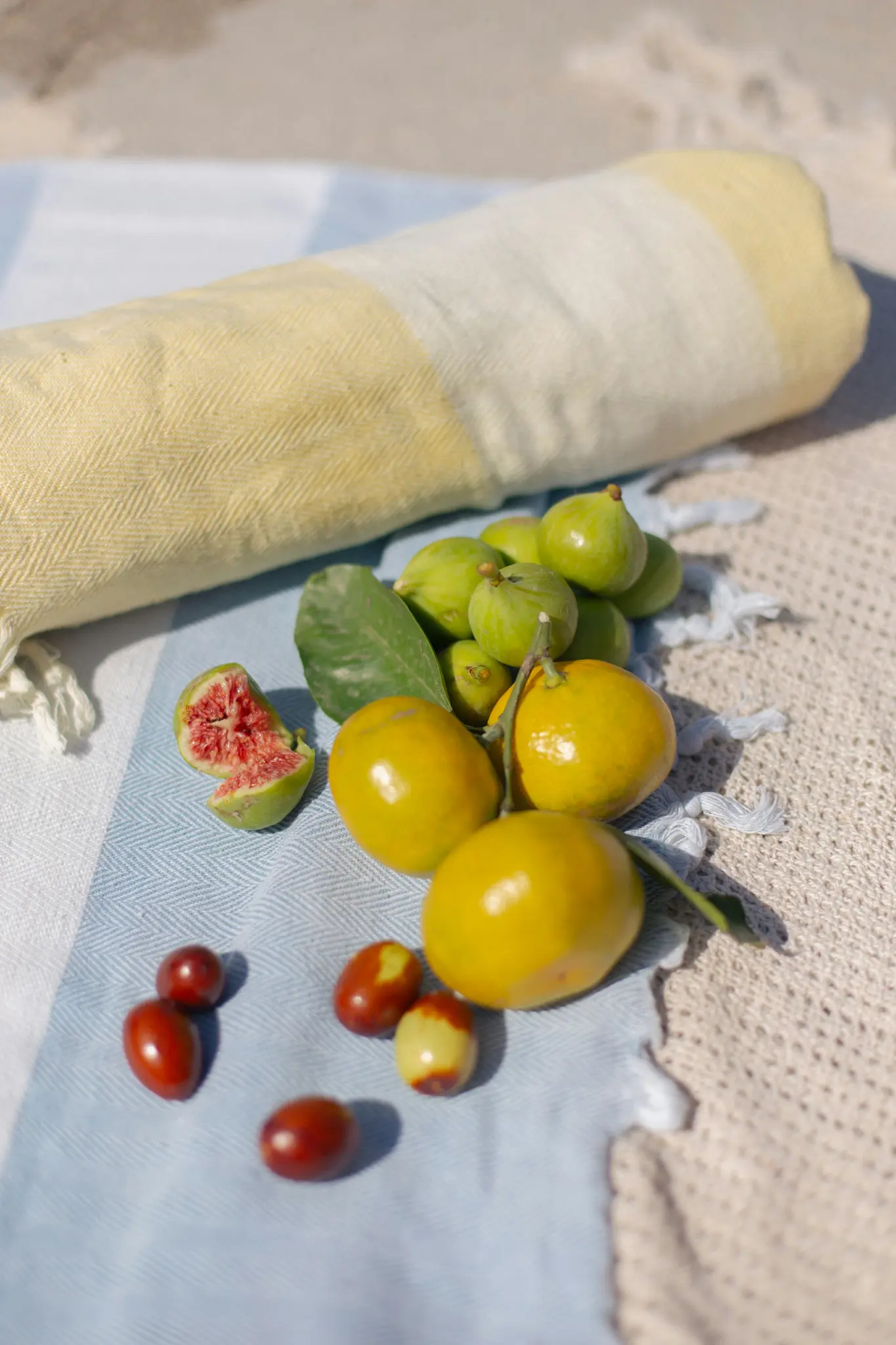 A close-up, high-angle shot of green figs, yellow mandarins, and red jujubes on a blue and white striped towel.