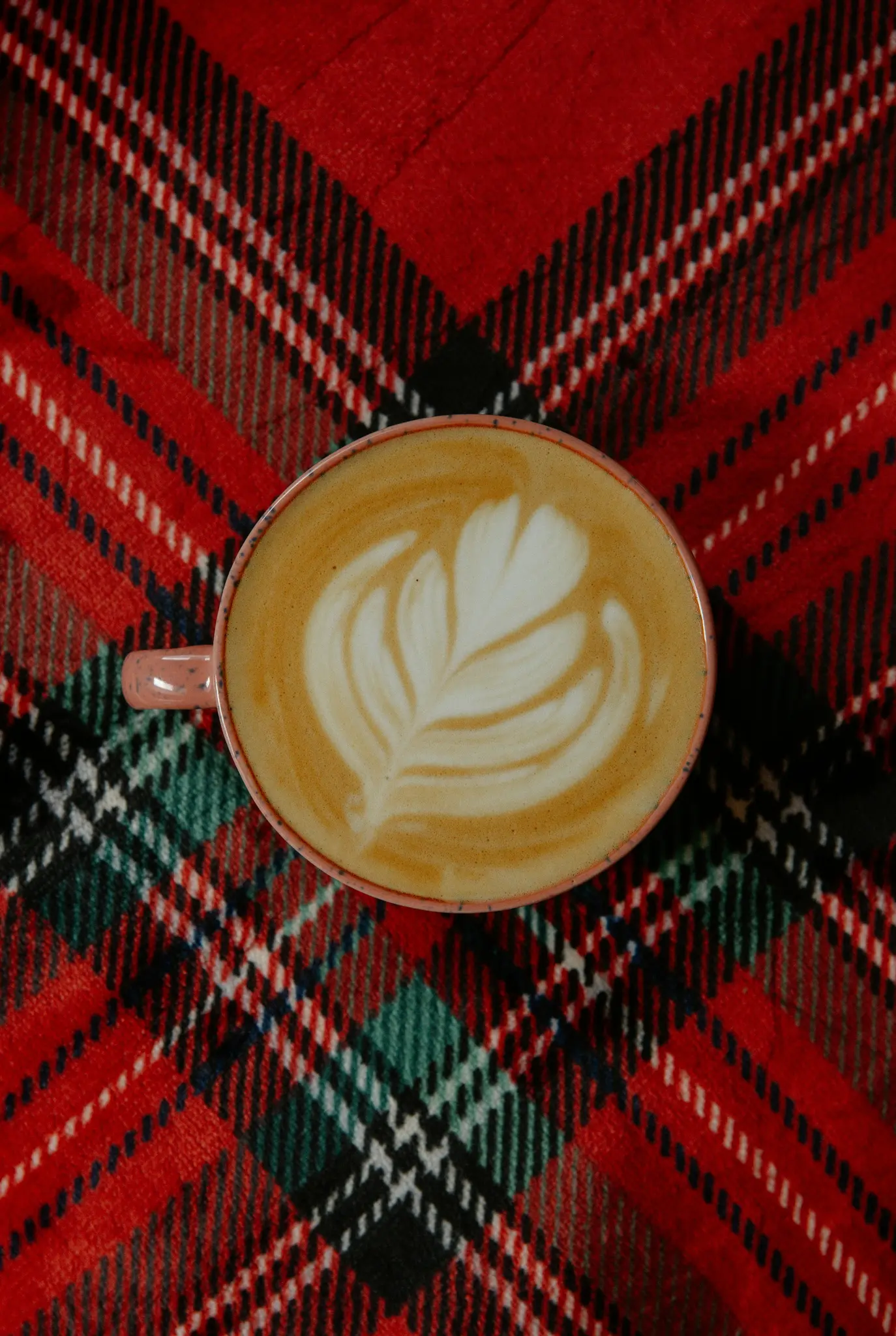 Een bovenaanzicht van een roze mok gevuld met een latte met ingewikkelde witte latte art, rustend op een rood, zwart en