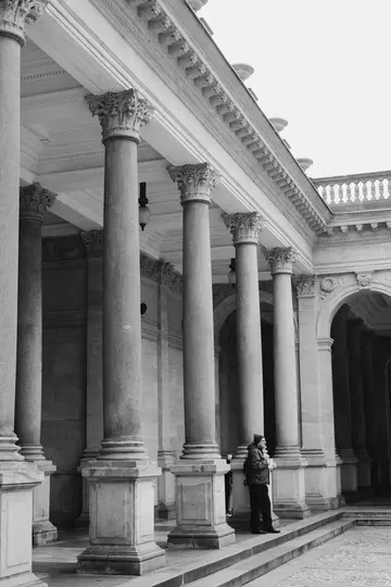 Una foto in bianco e nero mostra una persona in piedi su dei gradini accanto a un edificio imponente con diverse grandi