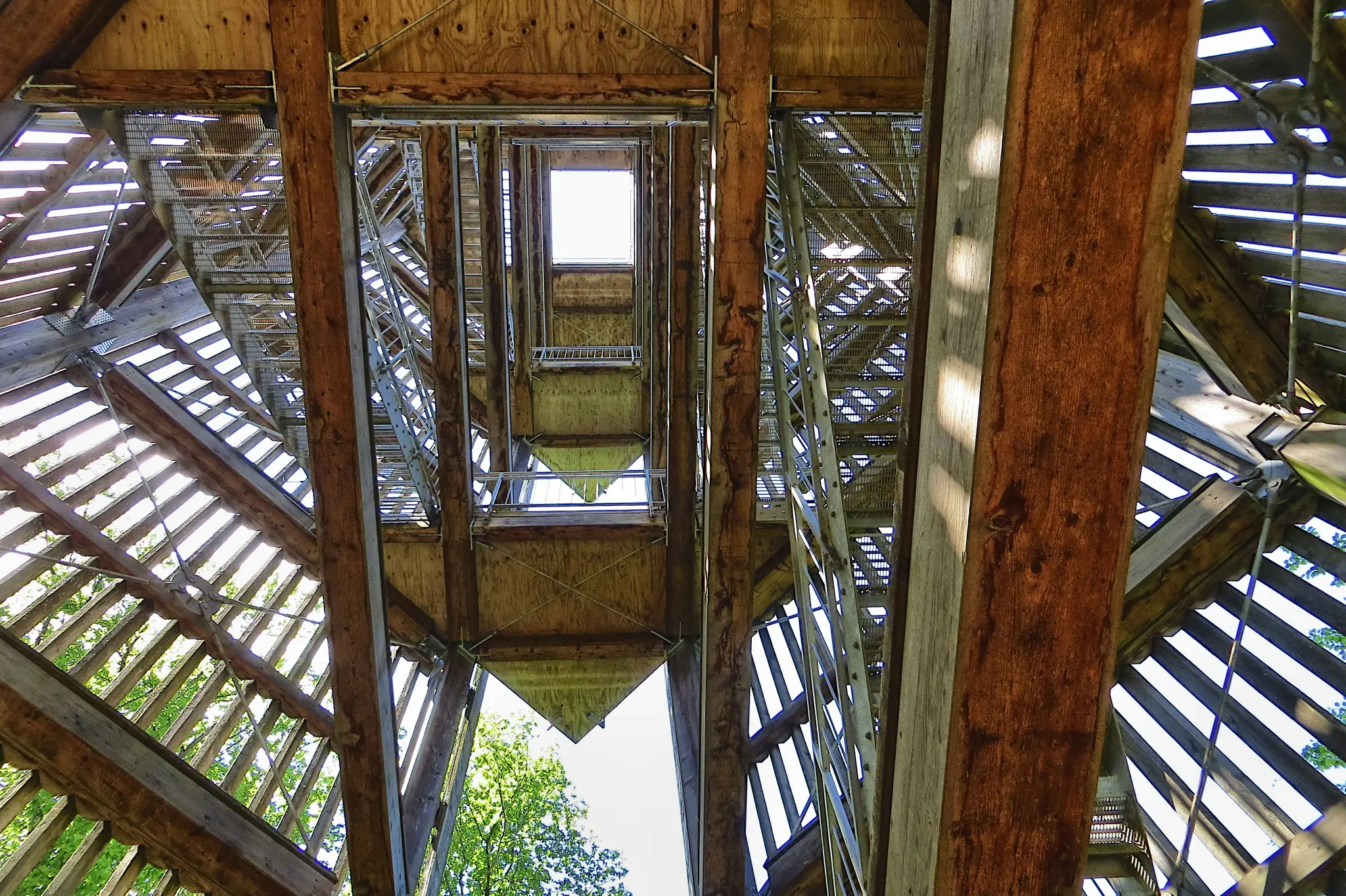A worm's-eye view looking up through the interior of a wooden observation tower, showing crisscrossing wooden beams and…