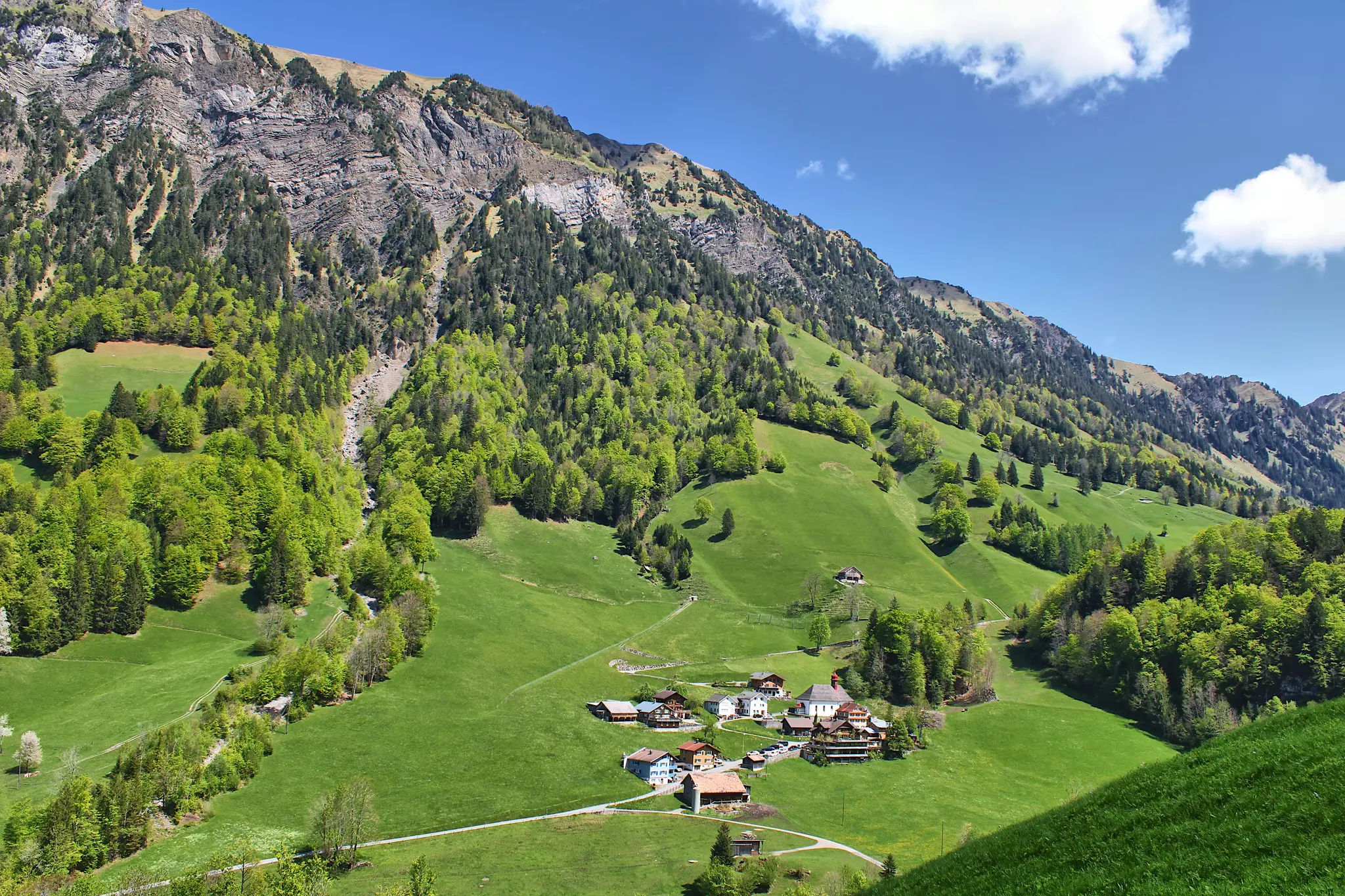 An aerial view of a small village with colorful houses and a church, situated in a lush green valley surrounded by steep…