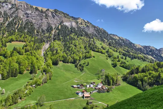 An aerial view of a small village with colorful houses and a church, situated in a lush green valley surrounded by steep…