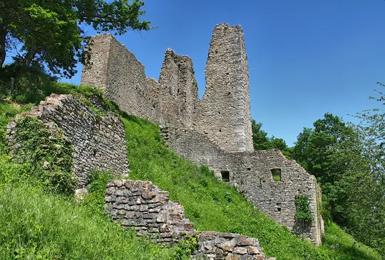 A low-angle wide shot of ancient stone castle ruins on a steep, vibrant green grassy hillside under a clear blue sky.