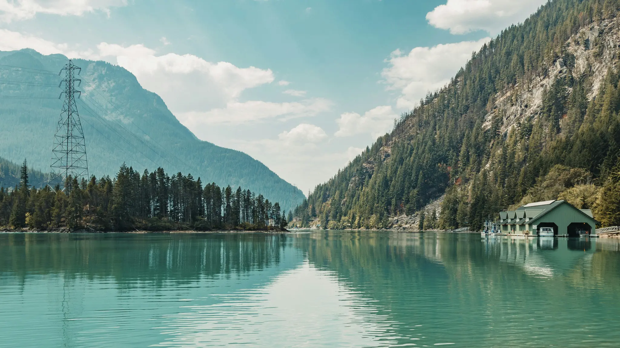 Une large photo de paysage d'un lac turquoise reflétant le ciel, bordé de montagnes escarpées et boisées. Une remise à