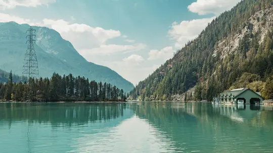 Une large photo de paysage d'un lac turquoise reflétant le ciel, bordé de montagnes escarpées et boisées. Une remise à