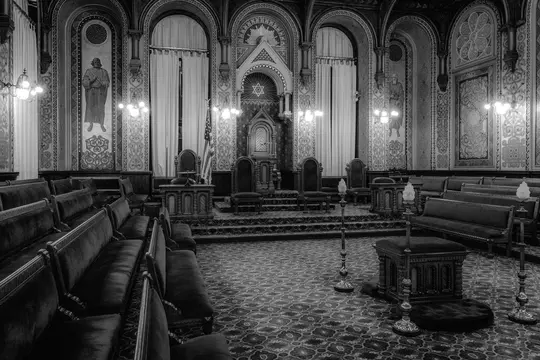 Une photo en noir et blanc d'une salle vide et ornée avec des rangées de bancs sombres faisant face à une estrade centrale
