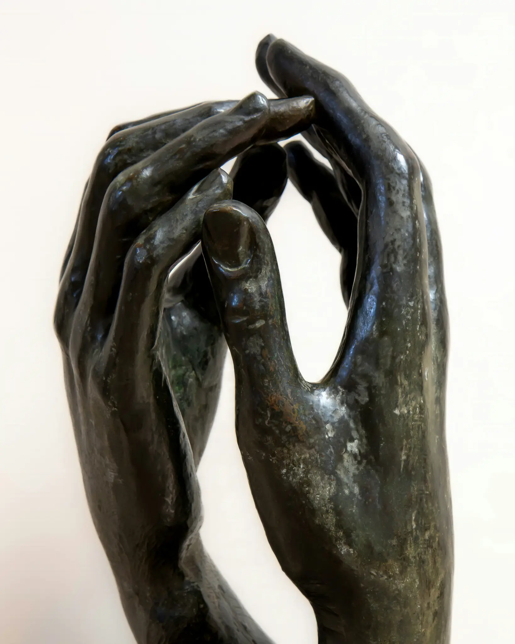 Gros plan, prise de vue verticale d'une sculpture en bronze sombre représentant deux mains aux doigts entrelacés, sur un fond