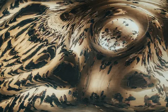 A close-up, abstract photo of a highly polished, curved metallic surface reflecting numerous distorted figures of people.