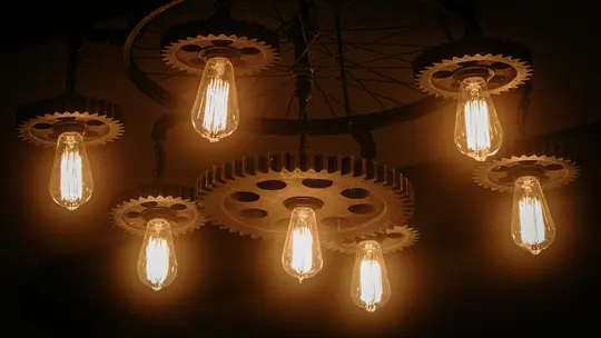 A close-up, low-angle shot of a steampunk-inspired chandelier featuring multiple gears and glowing Edison bulbs.