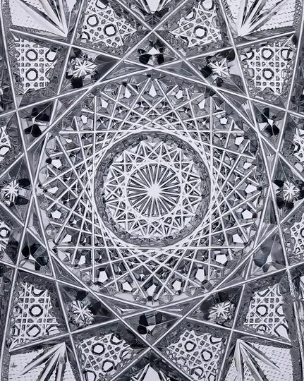 A close-up, abstract black and white photo of cut crystal glass, showing intricate geometric patterns and reflective…