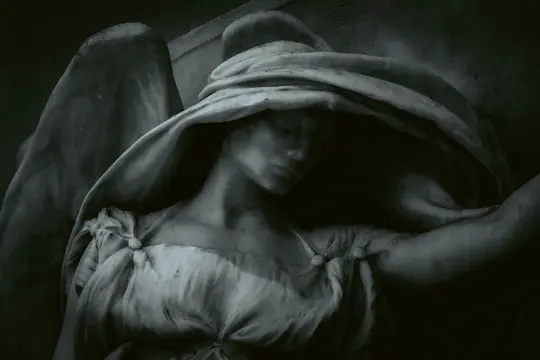Un gros plan sombre et mélancolique d'une statue d'ange en pierre. Le visage de l'ange est ombragé par une couverture de tête