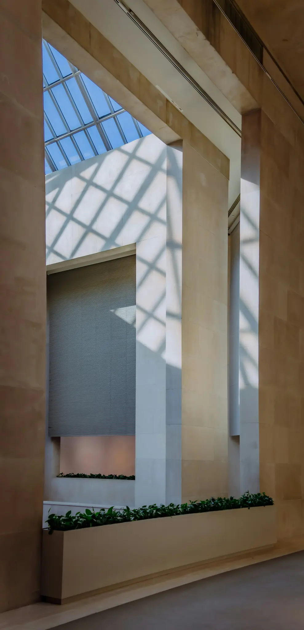 Un intérieur de bâtiment moderne comprend un puits de lumière en verre projetant des ombres en forme de diamant sur des murs