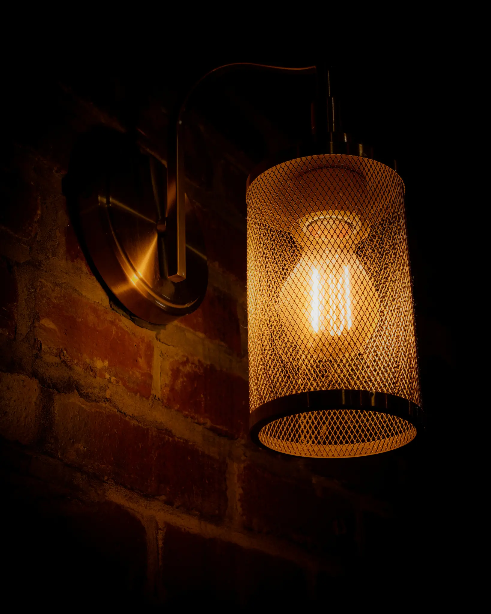 Gros plan d'un luminaire mural avec une ampoule Edison incandescente à l'intérieur d'une cage cylindrique en treillis