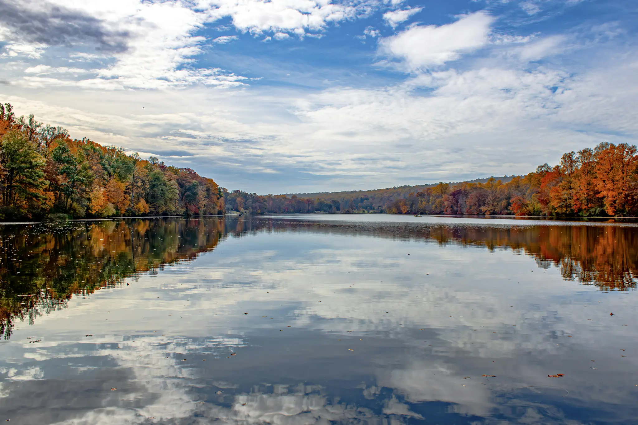 Une photo de paysage large d'un lac calme reflétant un ciel partiellement nuageux et des arbres d'automne colorés sur ses
