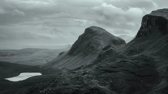 Une photo de paysage large en noir et blanc montre une chaîne de montagnes accidentée avec un petit lac de couleur claire