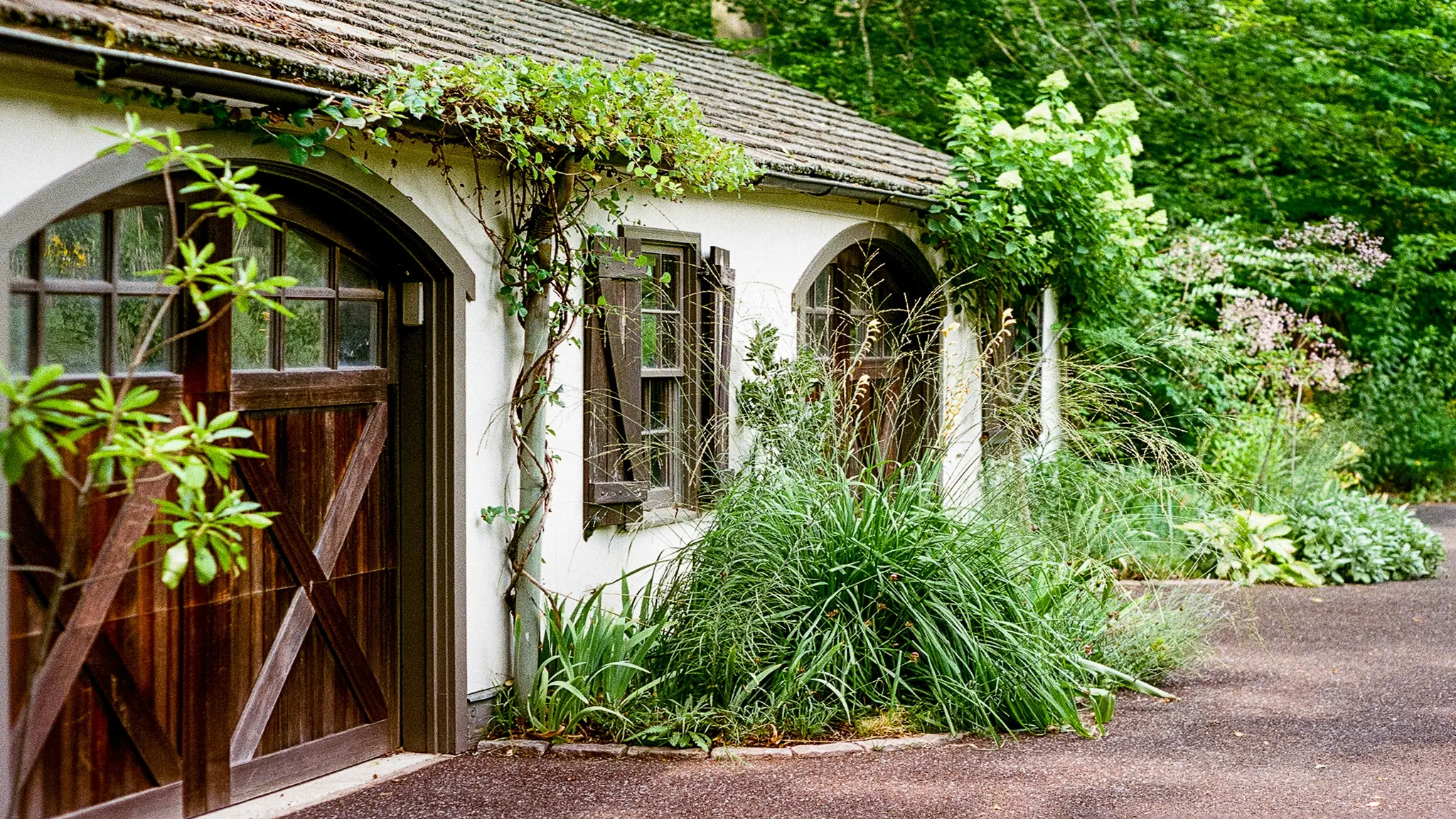 Un charmant bâtiment en stuc blanc avec un toit de tuiles brunes, des portes en bois cintrées et des fenêtres avec volets