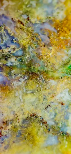 Živá makrofotografia povrchu minerálu alebo horniny, zobrazujúca zložité vzory žltej, zelenej, modrej a bielej.